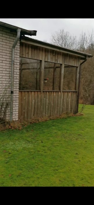 Halvt inglasad uteplats med tak och träväggar som ligger plant mot marken vid ett hus.