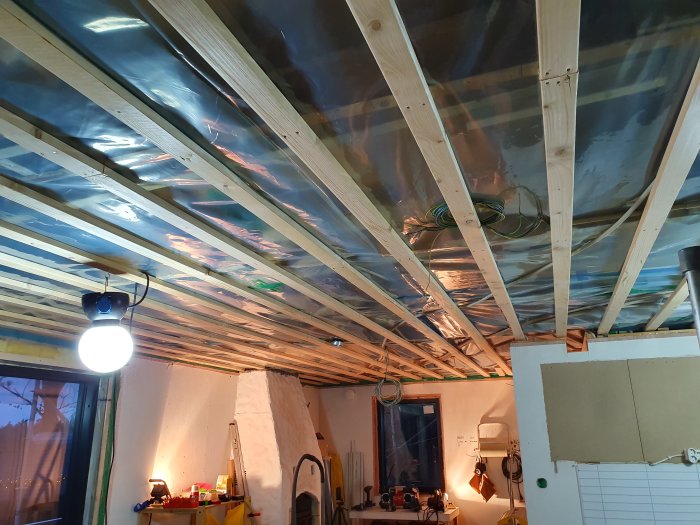 Renoveringsarbete på tak med exponerade träbjälkar, plastfolie, isoleringsmaterial och elinstallationer.