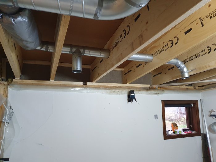Renoveringsarbete under tak med ventilationssystem, isolering och synliga träbjälkar inomhus.