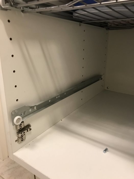 Inuti ett skåp med en monterad ledstång och ett gångjärn, samt en lös skruv på skåpets bottenyta.