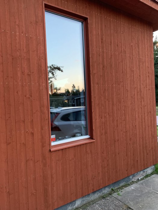 Nyinstallerad röd träpanel på husvägg med fönster och ofärdig sockel vid skymning.