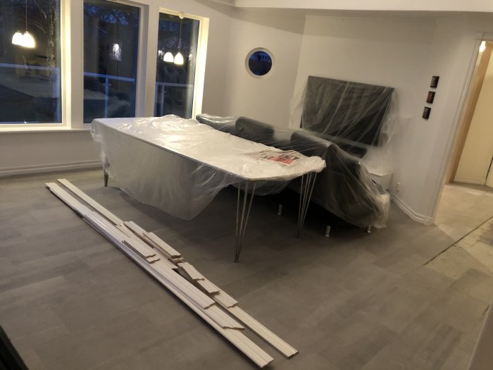 Renoverat rum med fogat golv och material för garderobsinbyggnad, skyddad möbel i bakgrunden.