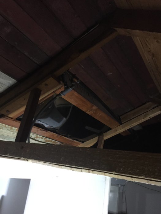 Öppet takstolsområde i kolonistuga med synlig vattentank under plåttak.