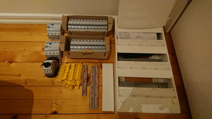 Elektriska byggkomponenter som säkringar och ledningar på ett trägolv, med överraskning över storleken.