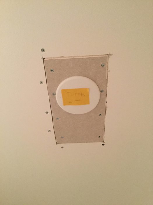Rektangulärt hål med fördelningsdosa och skruvar i nyligen renoverat badrumstak.