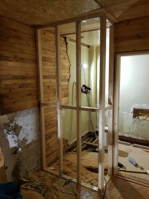 Renoveringsarbete med halvfärdig väggkonstruktion i trä och rörigt golv med byggavfall.