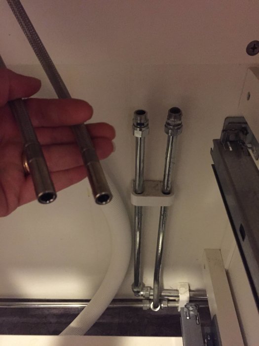 Hand håller två avkopplade metallslangar nära anslutningar under en diskbänk.