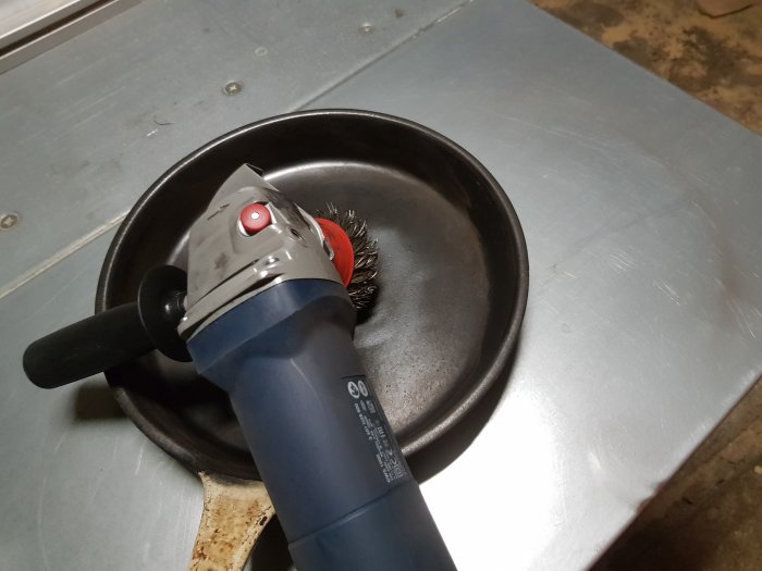 Elektrisk borrmaskin med borsthuvud i en rengjord stekpanna på ett metallbord.