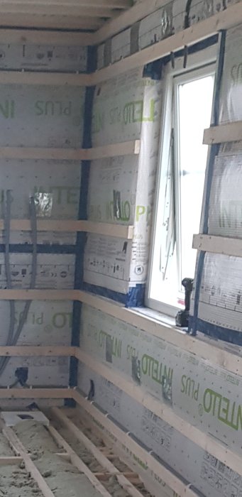 Ett pågående byggprojekt av en husövervåning med OSB-skivor och synliga reglar nära fönstret.