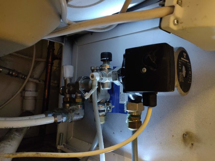 VVS-installation under varmvattenberedare med cirkulationspump, rör och ventiler.