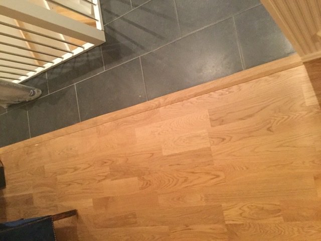 Nytt parkettgolv med synlig skarv mellan två golvlister vid övergången till klinkergolv.