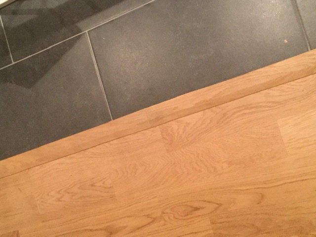 Övergång mellan parkettgolv och klinkergolv med en synlig skarv mellan två golvlister.