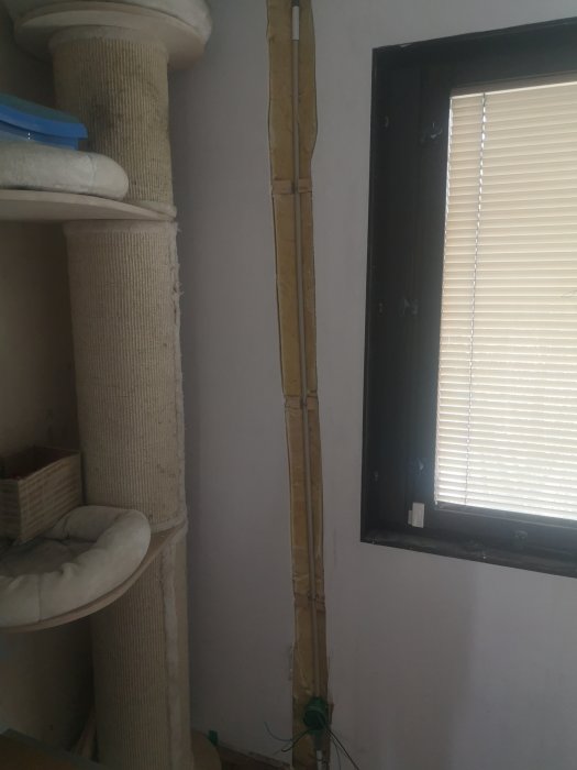 Öppen vägg som visar isolering och elinstallationer bredvid ett fönster i ett äldre hus.