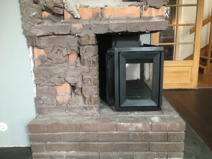 Nyinstallerad kassett i en ofärdig tegel öppen spis med synlig murbruk och oslutlig yta.