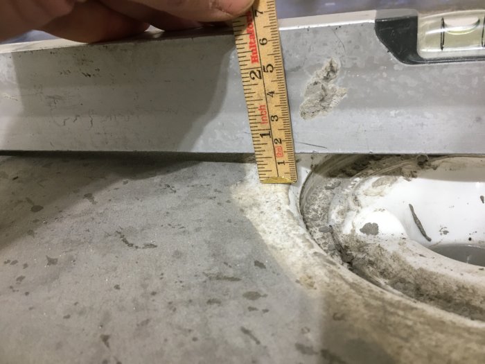 Mätning av golvnivåskillnad vid en duschbrunn med tumstock och vattenpass.