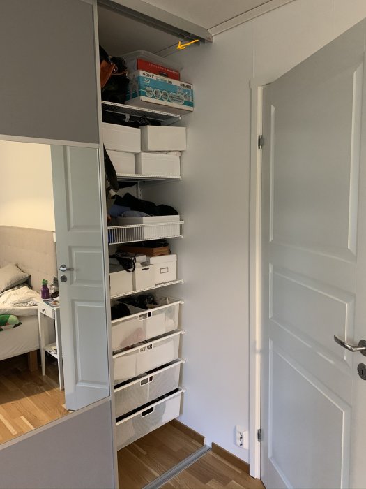 Bild på ett öppet garderobsskåp med skenor och lådor, orange pil pekar på en plats i taket för LED-slingans kabel.
