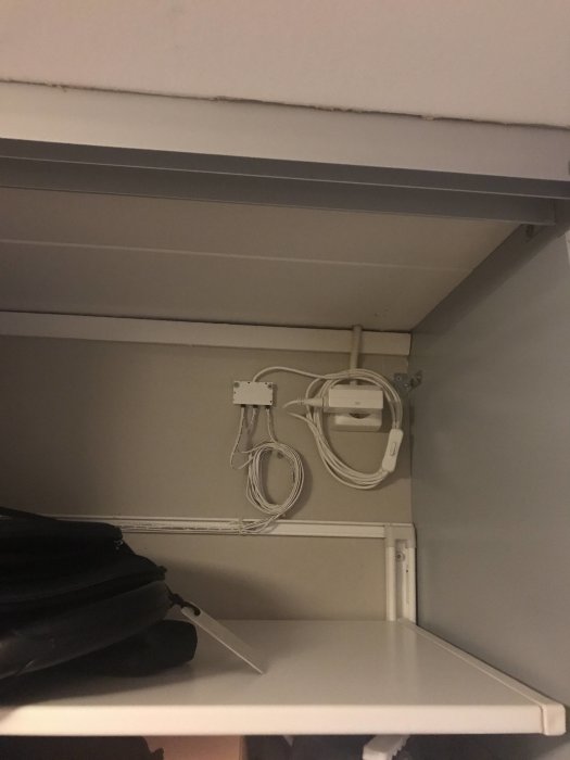 Eluttag placerat högt på väggen nära taket med kablar som löper längs med en hylle.