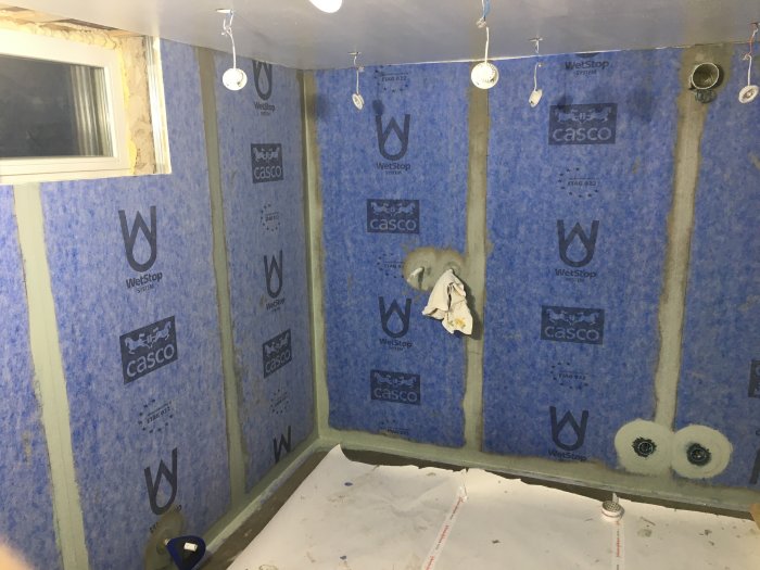 Ett halvfärdigt badrum med blå fuktspärrsfolie på väggarna och isolering synlig.