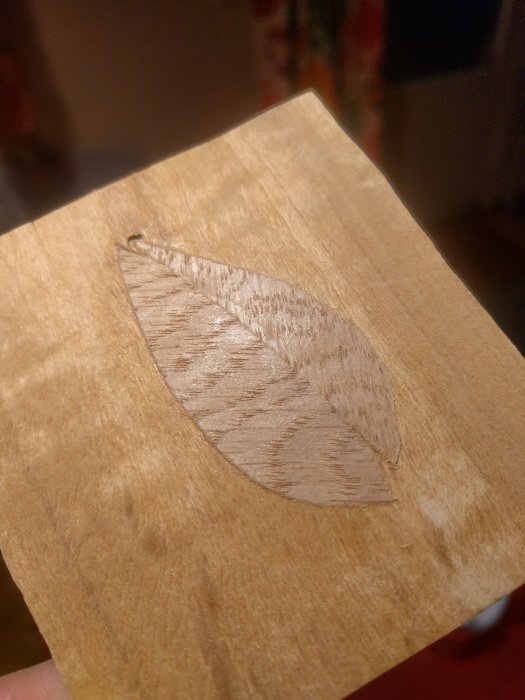 Ett träsnideri som föreställer en detaljerad intarsia lövform inlagd i ett trästycke.