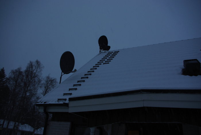 Tak med snö och två paraboler under mörk vinterhimmel.