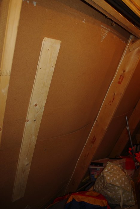 Vind med synliga takstolar och isolering samt förvarade föremål, fotograferad inomhus under vinter.