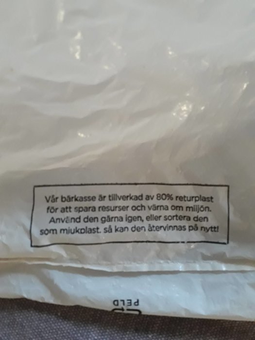 Närbild av text på Willys plastpåse som beskriver att påsen är tillverkad av 80% returplast och uppmaning till återanvändning.