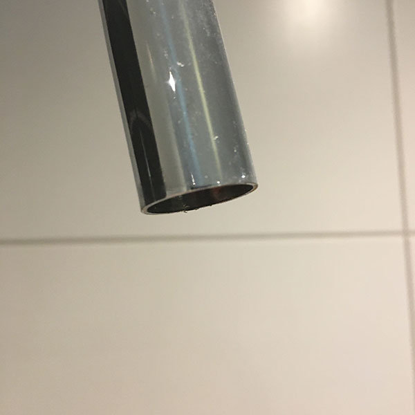 Korroderat överrör från en takdusch utan gänga mot en kakelväggsbakgrund.