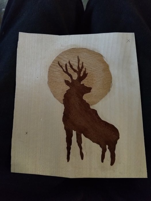 Intarsiaarbetet av en mörk hjort mot en ljus bakgrund med inlagd måne i träfaner.