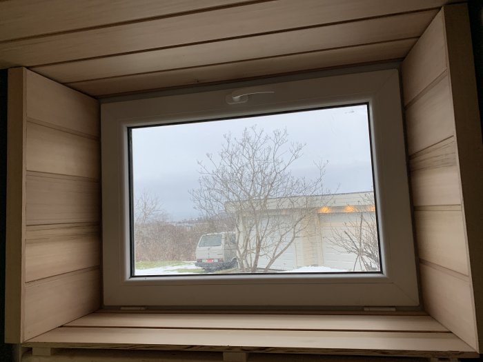 Färdigställt fönster med träpaneler runtom och utsikt mot träd och byggnad.