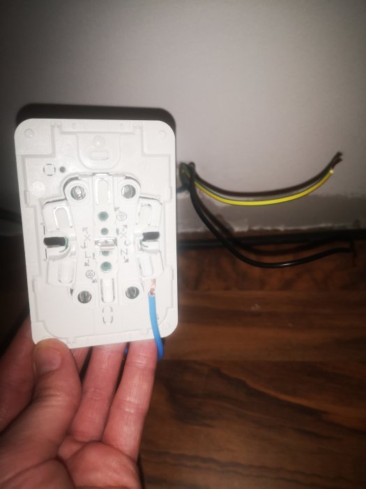 Hand som håller en elektrisk dosa med osammanfogade kablar och markerade ingångspunkter.