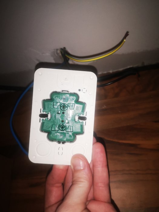 En person håller en osammanfogad elektrisk dosa med synliga kabelanslutningar och outtagna markeringar för kabelgenomföring.