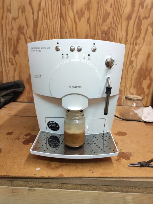 Siemens kaffemaskin i arbetsmiljö med ett glas kaffe under utkastet, droppbricka med vattendroppar.