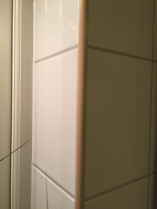 Gulnad hörnlist i ett badrum intill vita kakelplattor som visar ålderstecken.