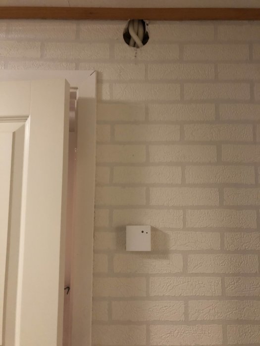 Vitt tegelvägg med dolt rör i kanal och isolering, och en tempgivare installerad på väggen.