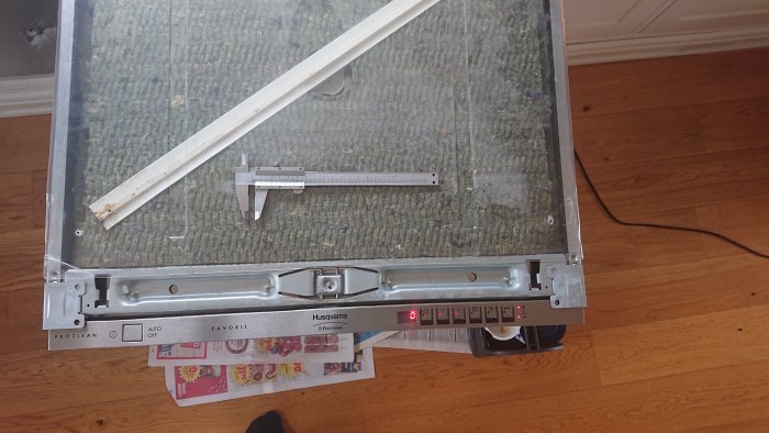 Inbyggd diskmaskin framdragen för undersökning, med synlig undersida och front.