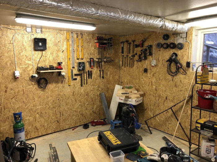 Verkstadsgarage med nyinstallerade osb-skivor på väggarna och verktyg upphängda, ouppackat byggmaterial synligt.