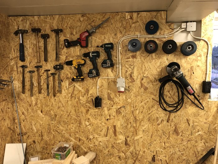 OSB-skivor på vägg i garage med verktyg ordnade på väggen och slipmaskindiskar upphängda.