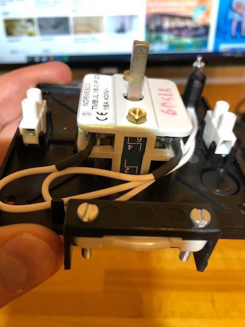 En hand håller en elektrisk brytare med etiketter och vit kablage synlig.