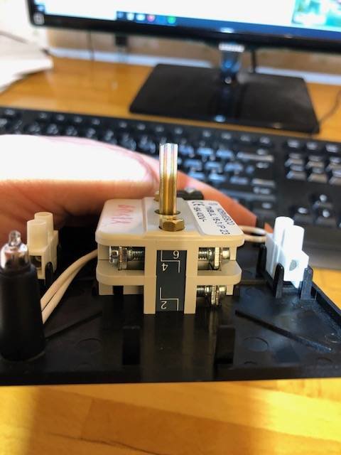 Hand håller en elektrisk brytare med numrerade anslutningar, synlig märkning, och frågor om installationen.