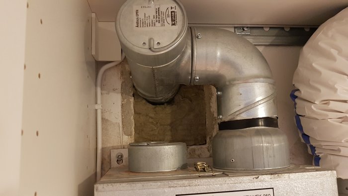 Ventilationskanal med isolering i en öppning bredvid ett avluftsrör i ett kök.
