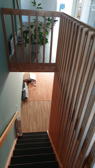 Öppen trätrappa med svarta plansteg och spaljé på övervåningen, samt diverse föremål på golvet.