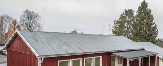 Baksidan av ett rött hus med ett plåttak som visar tecken på rost, i behov av sandpappering och tvätt inför målning.