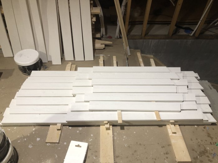 Nymålade vita träplankor upplagda för torkning i en verkstadslokal.
