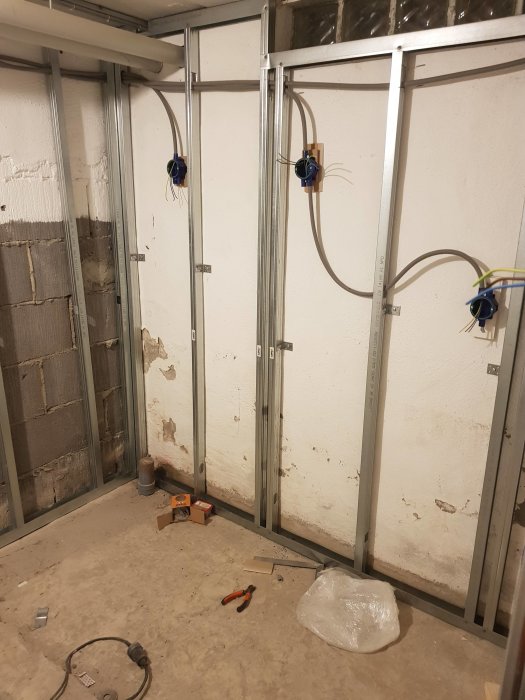 Renoveringsrum med golv och väggstommar förberedda för våtrum med synliga avlopps- och vattenledningar.