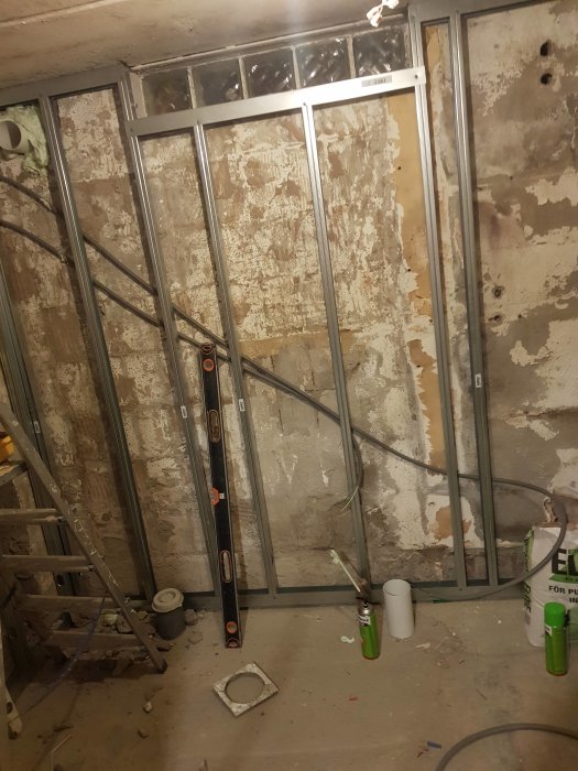 Renoveringsarbete med nya golvramar och synliga rörledningar i ett blivande våtrum.