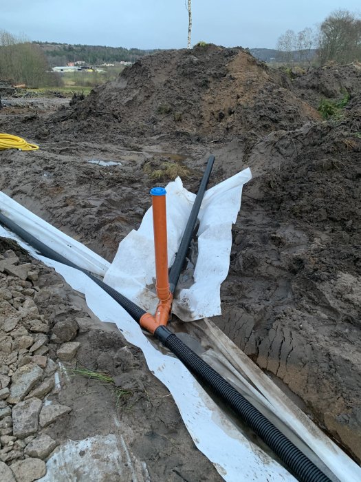 Installation av dräneringsrör med omgivande grävd jord och markduk på byggplats.