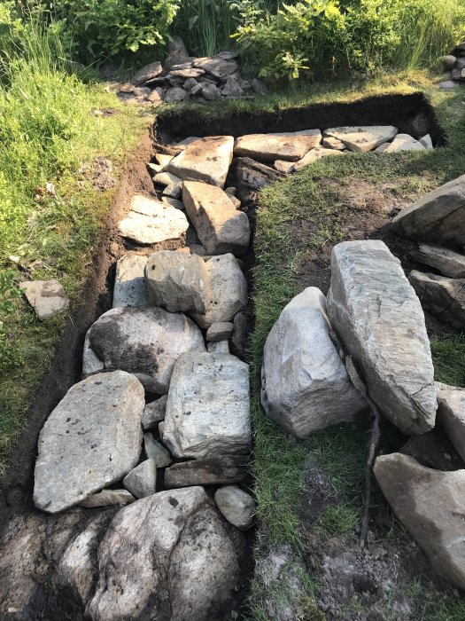 Stora stenar på gräsmatta, indikerar början på byggandet av en grillplats.