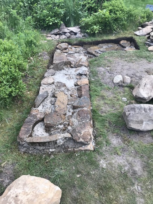 Början på en hemmabyggd grill av sten och murbruk på en gräsmatta.