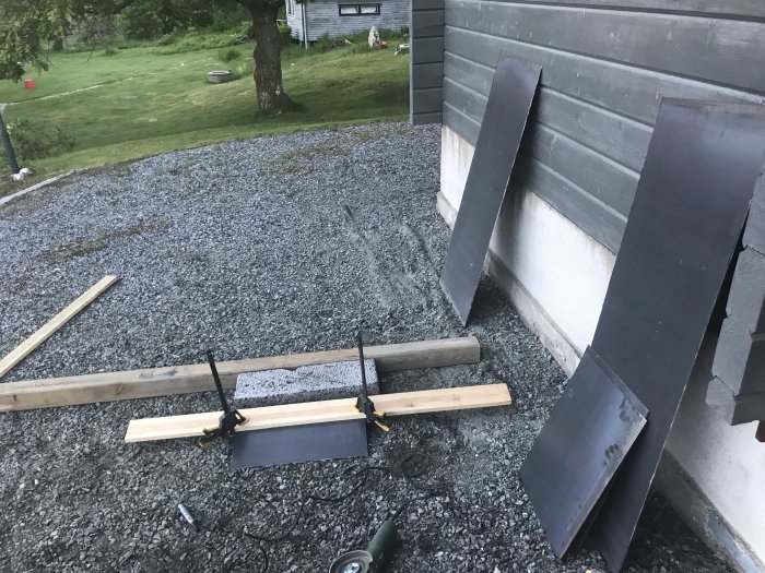 Ihopsvetsade cortenplåtar vid husvägg på grusunderlag, avsett för bygge av grill och rök.