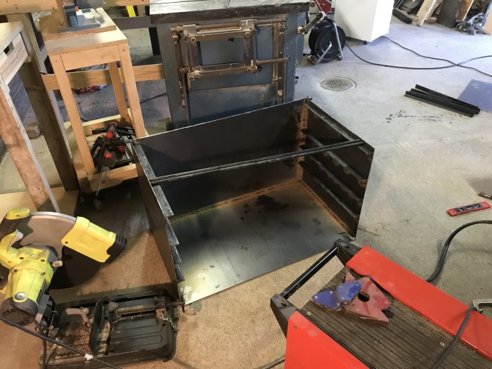 Svetsade cortenplåtar för en hemmagjord grill i ett verkstadsrum med verktyg.